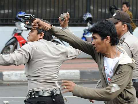 Seorang pegawai polis berpakaian preman mengacukan pistol ke arah para penunjuk perasaan manakala pegawai polis yang lain melemparkan batu. - Foto AFP