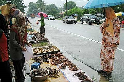 Seorang penjual ubi kayu Faezah Hassan (kiri) menjual ubi kayu di tepi jalan antara Jalan Kampung Batu Enam - Kuala Terengganu dekat Kampung Kubang Jela di Kuala Terengganu, kepada seorang pelanggan pada musim tengkujuh yang berlaku di negeri itu sejak beberapa hari lalu. -foto BERNAMA